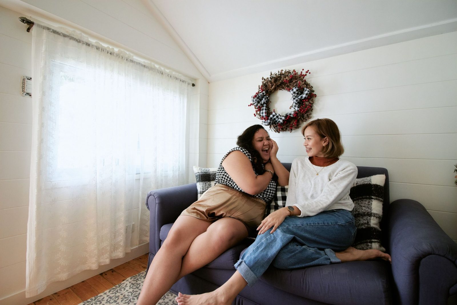 Zwei Frauen lachen zusammen auf dem Sofa eines hellen Wohnzimmers